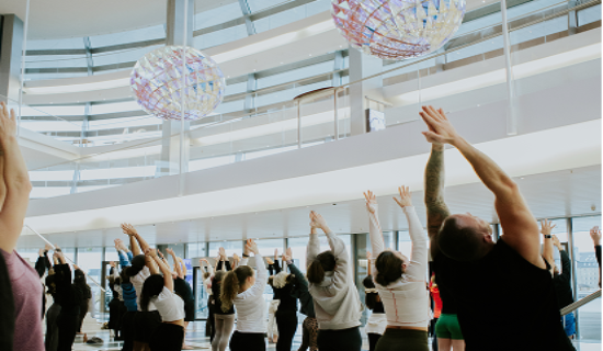 Group of people with arms raised in a modern building with colorful spherical lights.