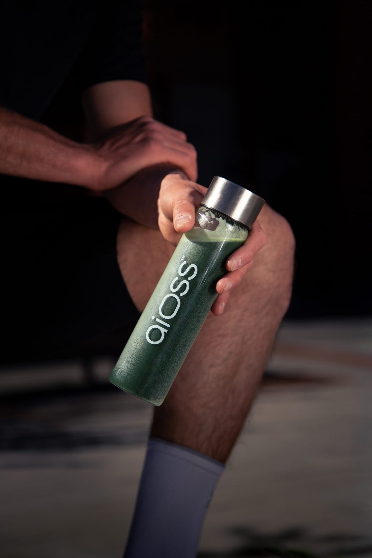 Hand holding an aioss bottle of green supplement drink
